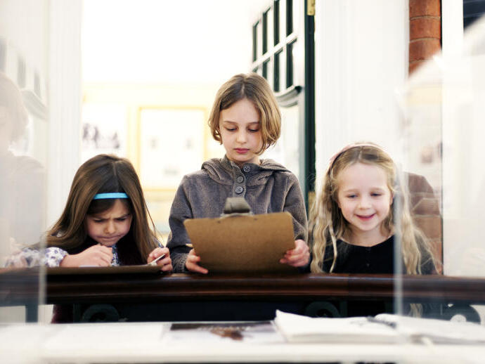 Three young girls study an exhibit in a glass display cabinet, in a museum.