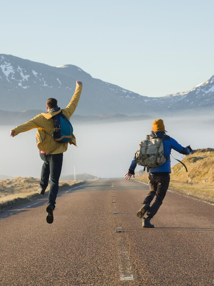 Due uomini che camminano e saltano su una strada circondata da montagne