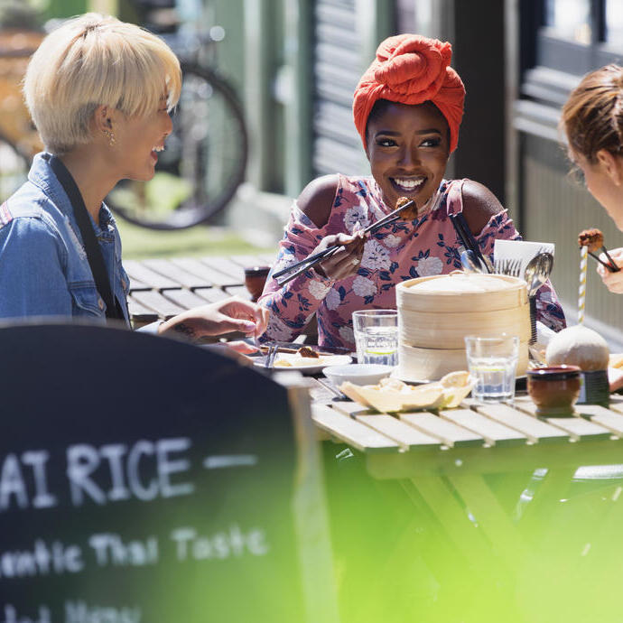 Three young women friends enjoying dim sum lunch at a sunny pavement cafe
