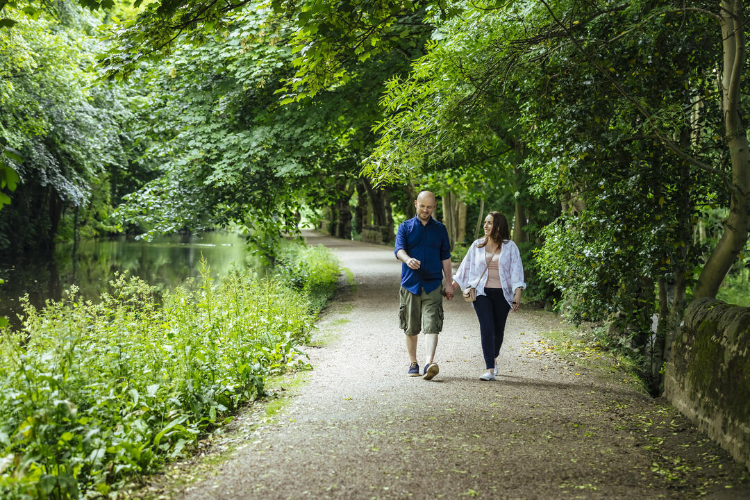 A man and a woman walk by a river with surrounding trees