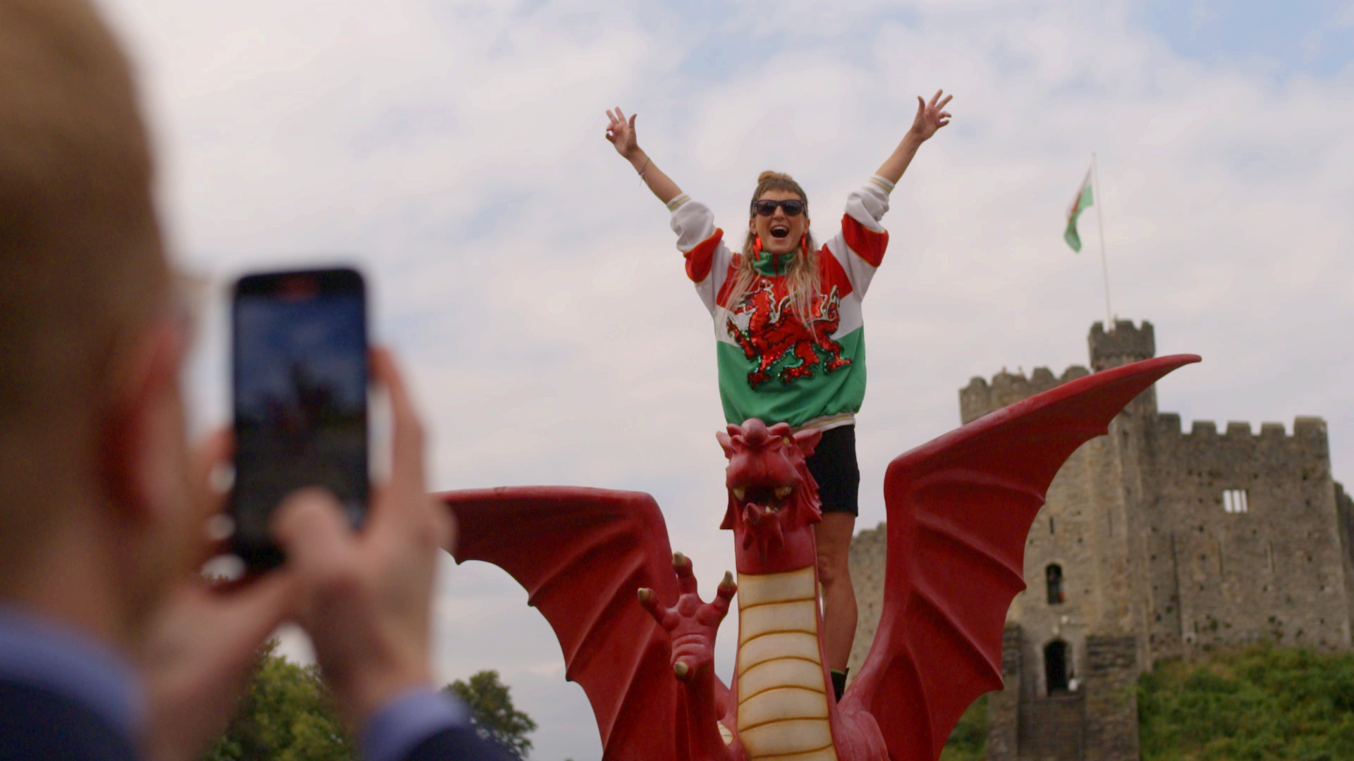 Woman standing with arms outstretched on a model Welsh dragon in front of a castle