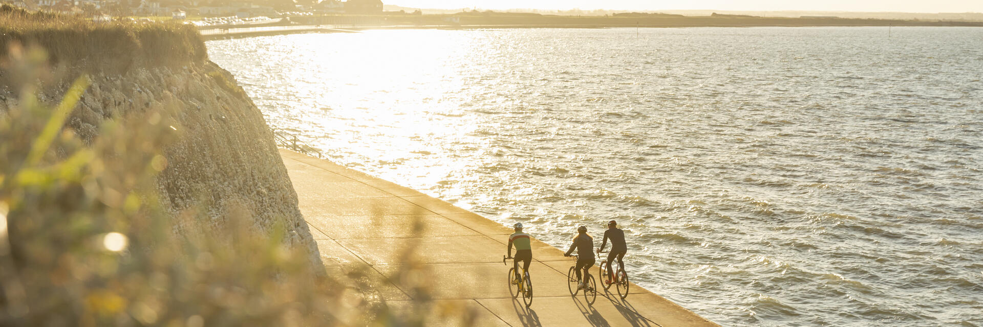Three cyclists on a coastal path during sunset