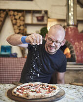 Man sprinkling cheese on pizza at a food market