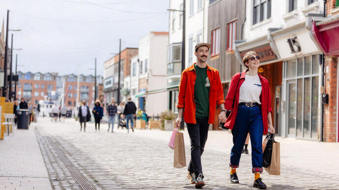 A man and a woman walk along a shopping street with bags