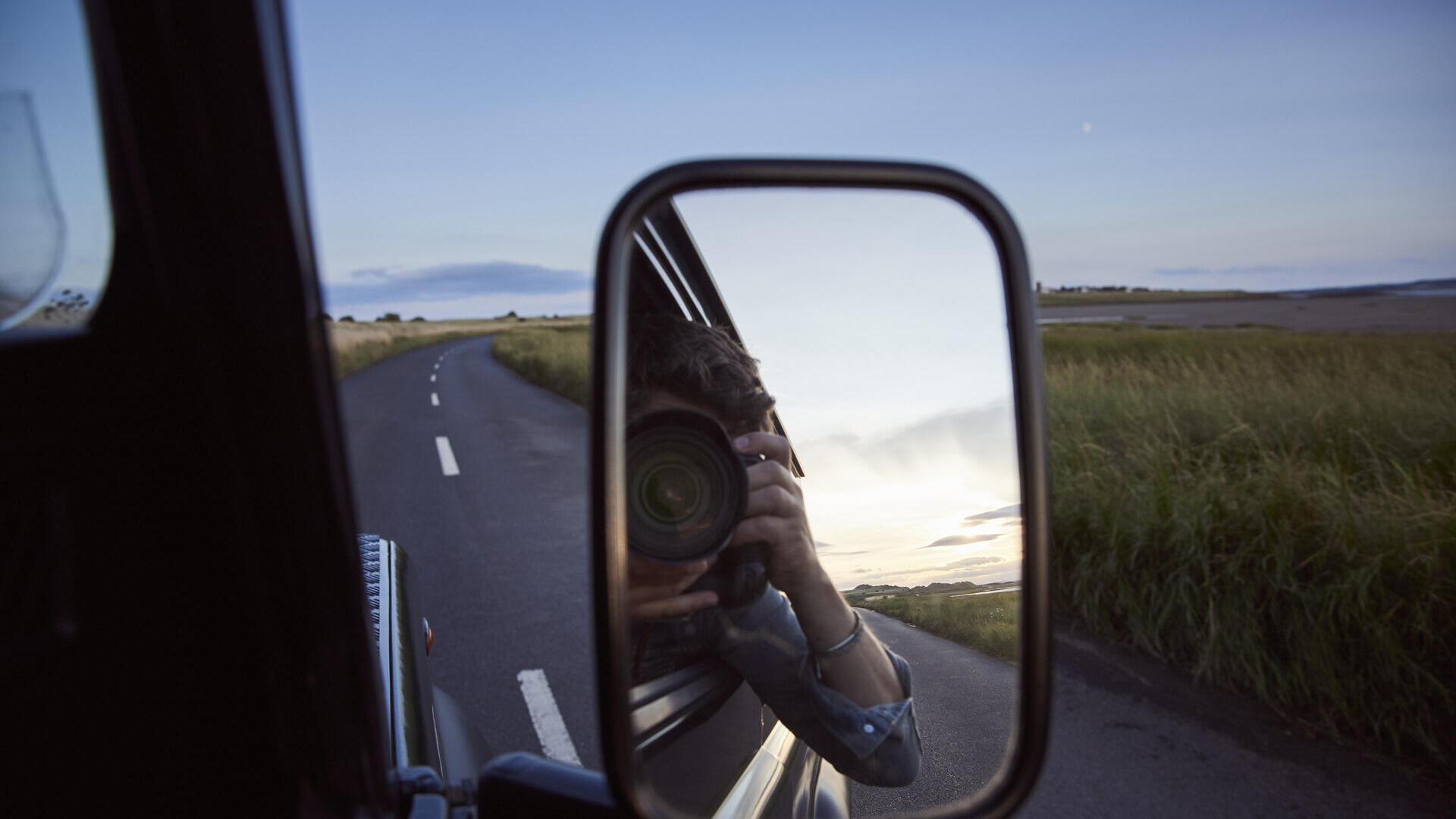 Reflet d'un homme avec un appareil photo dans le rétroviseur latéral d'une voiture
