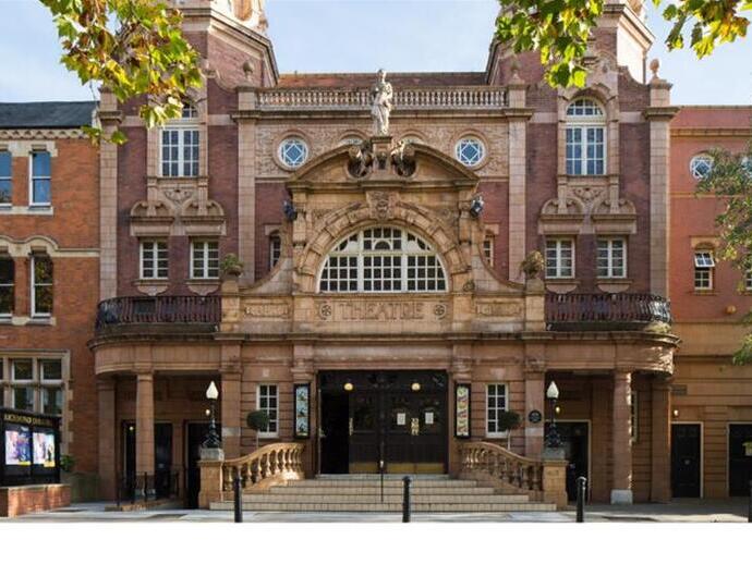 Fachada de un teatro histórico de ladrillo rojo con columnas, estatuas y detalles arquitectónicos.