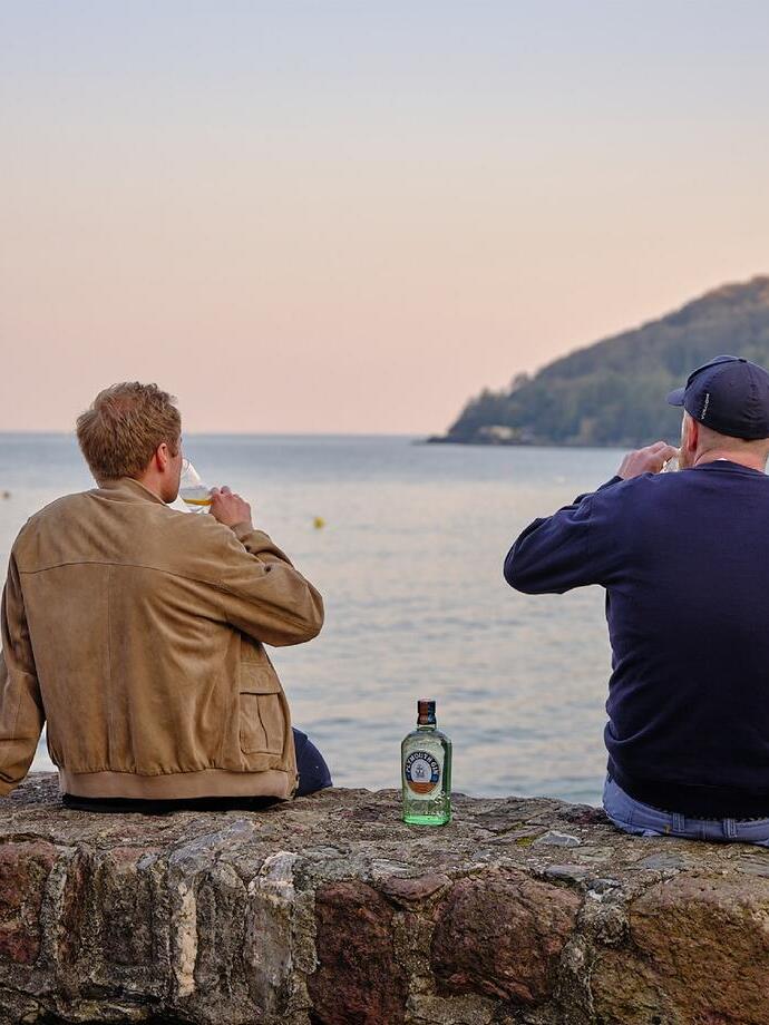 Dos hombres bebiendo ginebra mientras contemplan el mar