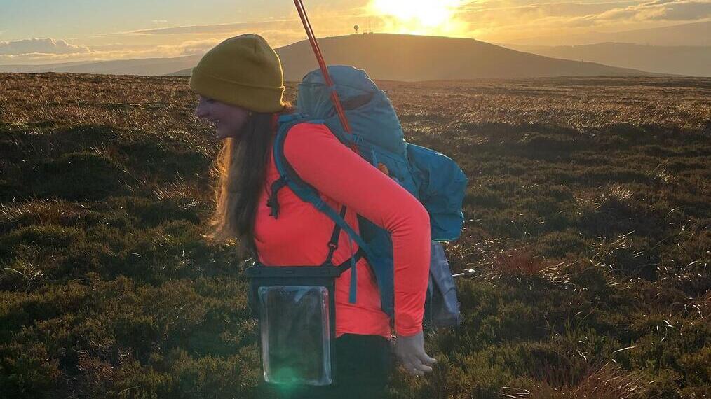 Female hiker with a backpack and walking poles, hiking through the countryside of Kilder in Northumberland at sunrise