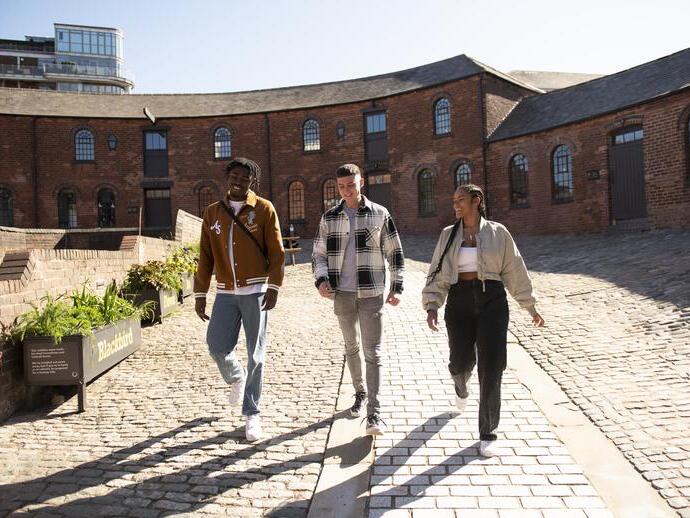 Tre amici che camminano davanti a vecchi magazzini industriali su una strada acciottolata