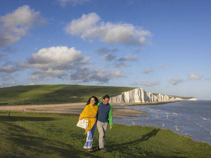 Una pareja camina junta por un promontorio con acantilados de creta blanca al fondo.