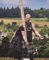 امرأة ترتدي تنورة اسكتلندية تتعلم كيفية رمي جذع الشجرة مع مدرب ذكر