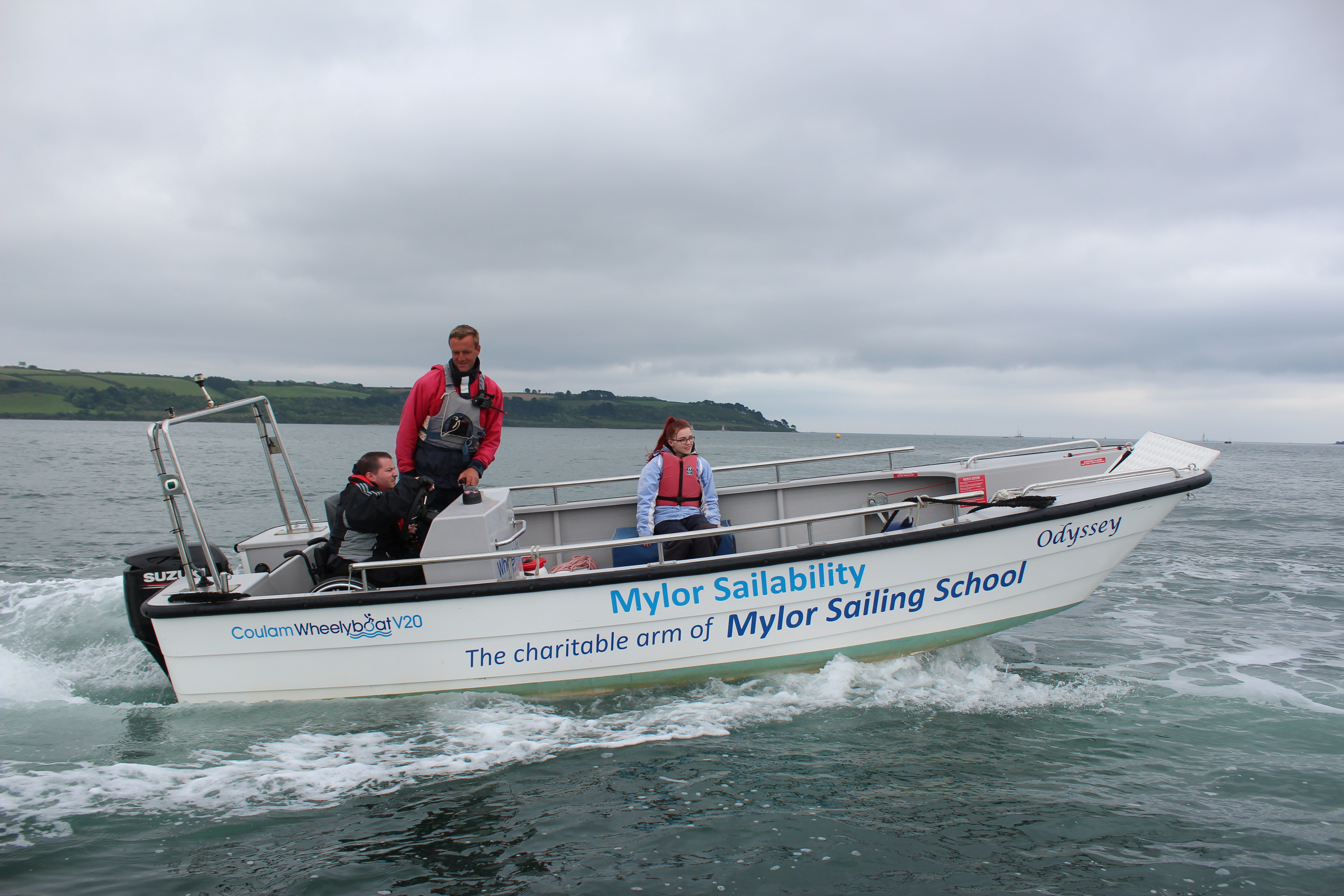 Uomo su una sedia a rotelle che guida una barca in mare accompagnato da un istruttore e da una donna