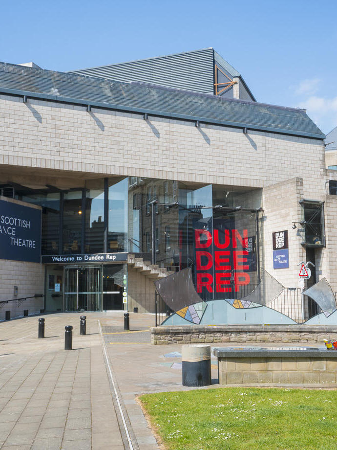 Exterior view of the Dundee Rep theatre with a person sitting outside on a bench.
