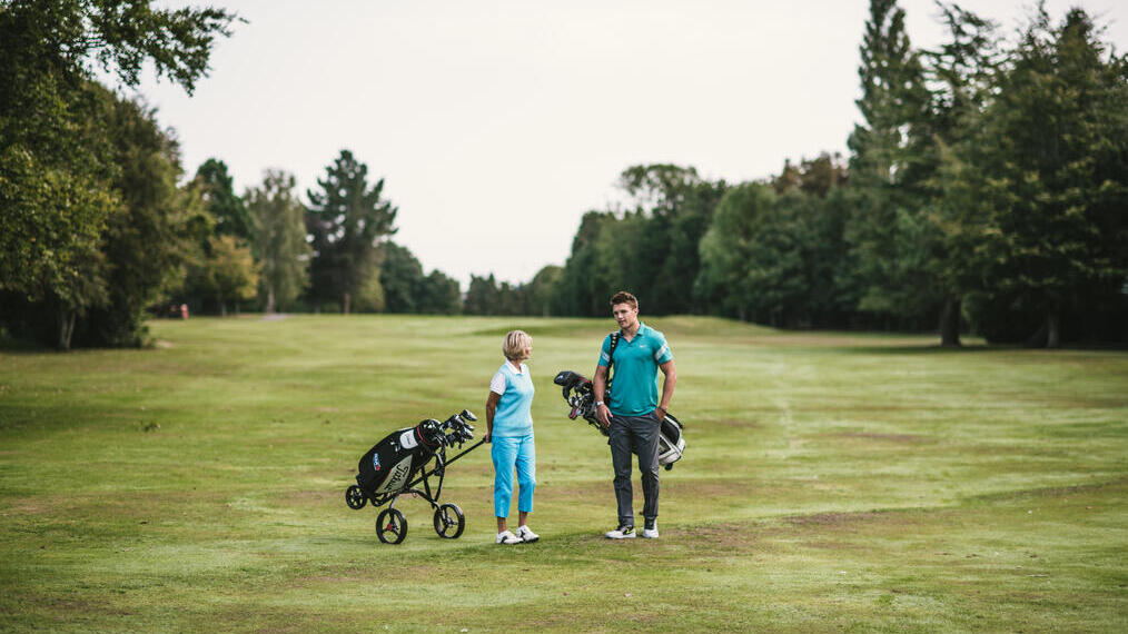Ein Mann und eine Frau tragen Golfschläger auf einem Golfplatz