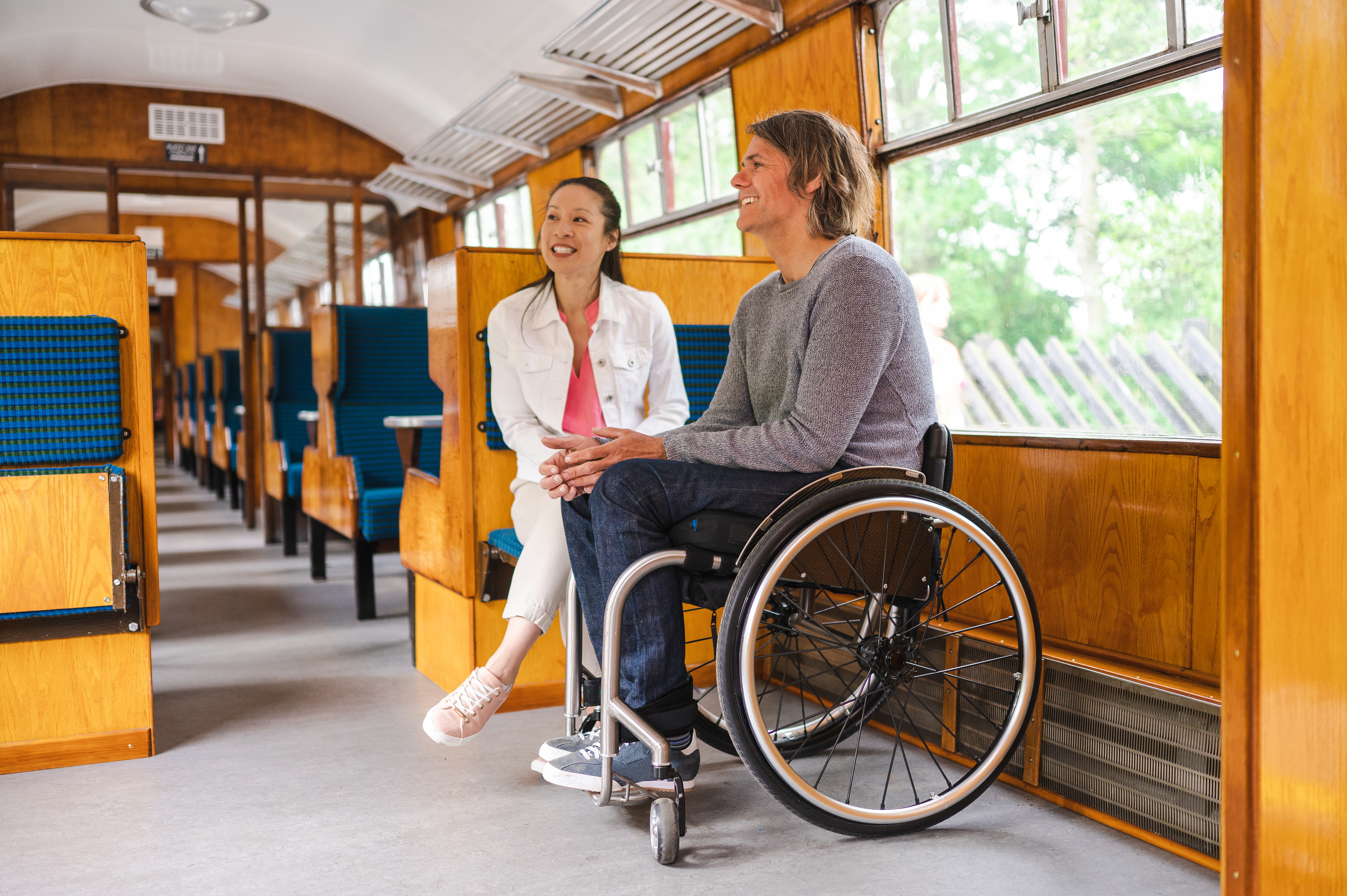 Man sitting in a wheelchair next to woman sitting on seat in accessible carriage on heritage train