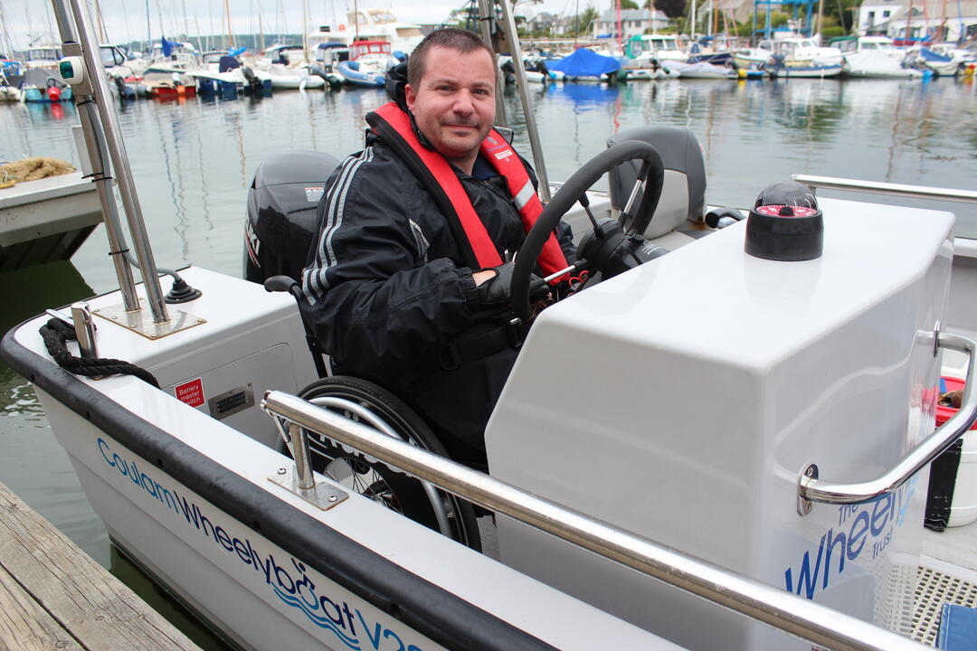 Man in a wheelchair steering a wheelyboat and wearing lifejacket