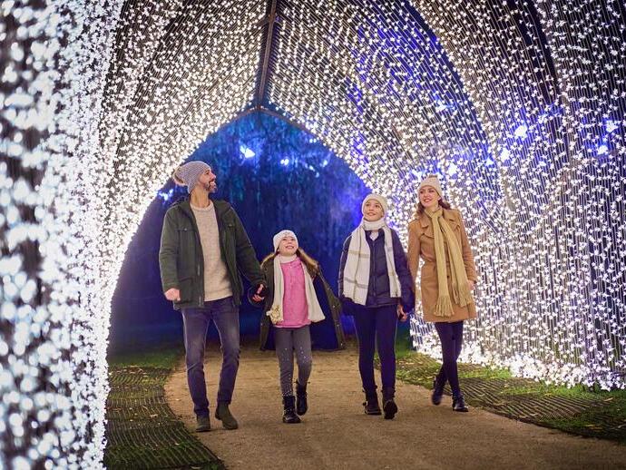Family with children walk under a Christmas lights archway