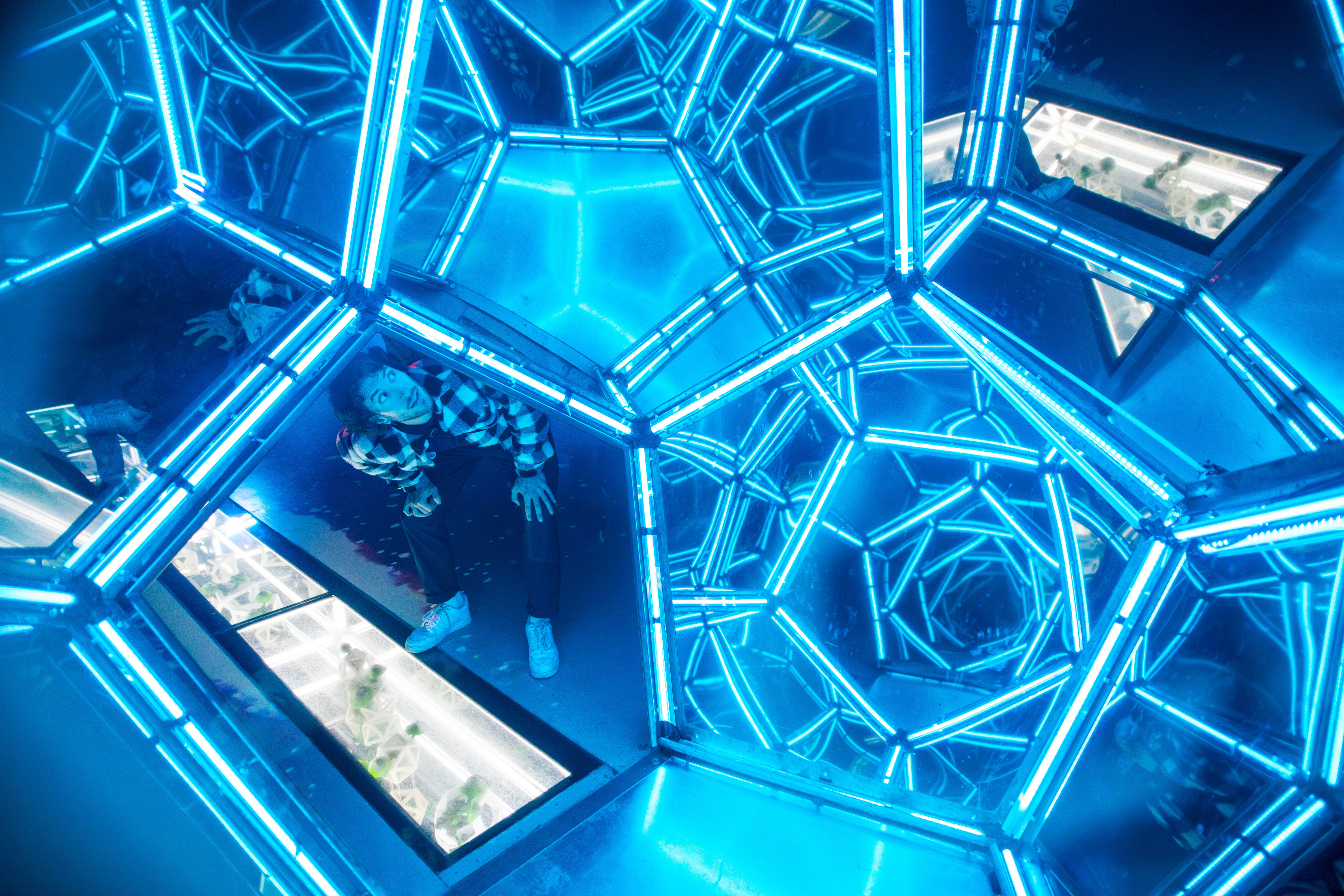 Personne dans une installation artistique avec miroirs et éclairage bleu, créant de nombreux reflets dans la scène.