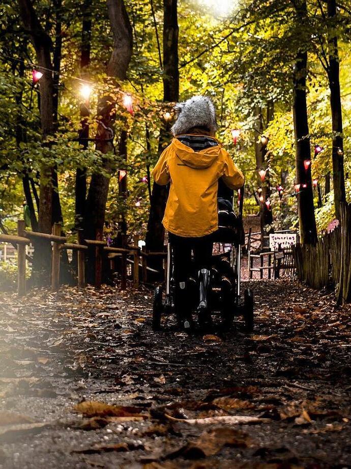 Person in Regenmantel schiebt einen Kinderwagen auf einem Waldweg