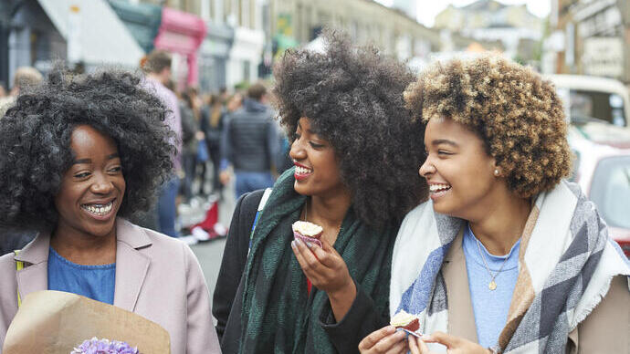 Three women laughing in a city street while eating cupcakes
