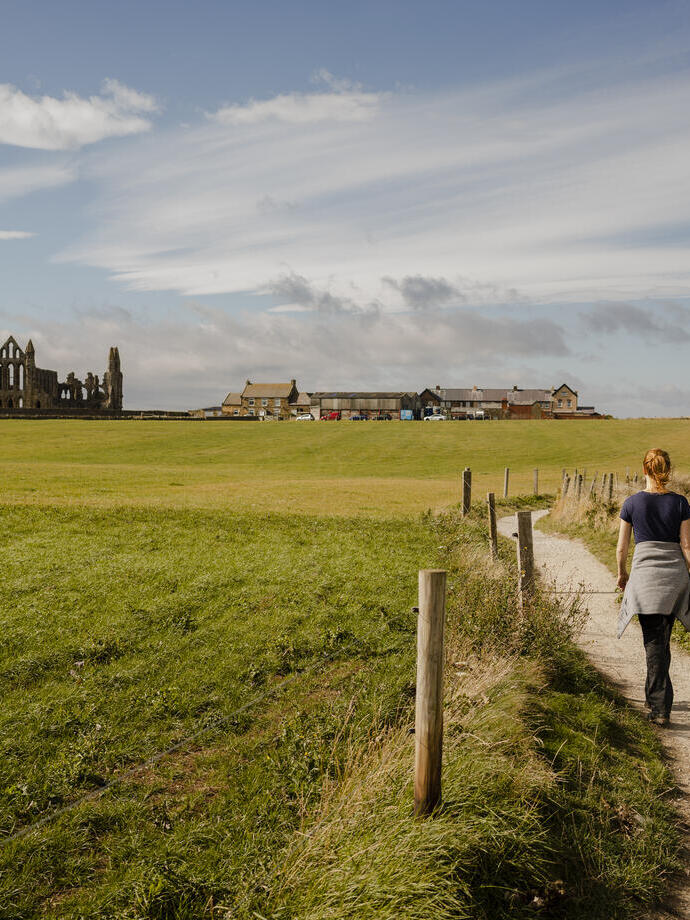 Femme marchant le long d'un sentier côtier vers une abbaye en ruines