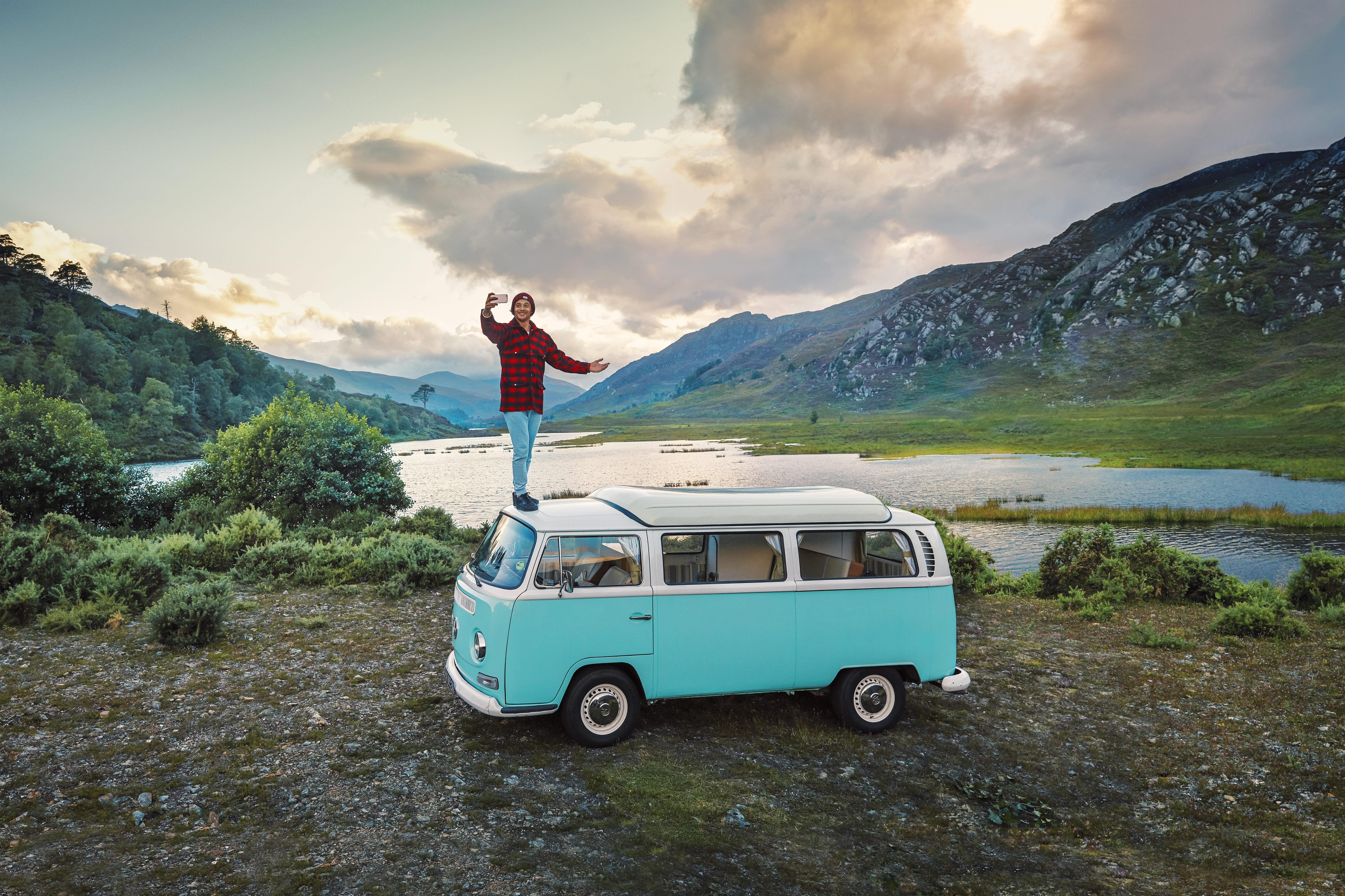 Man standing on camper van taking a selfie on the shore