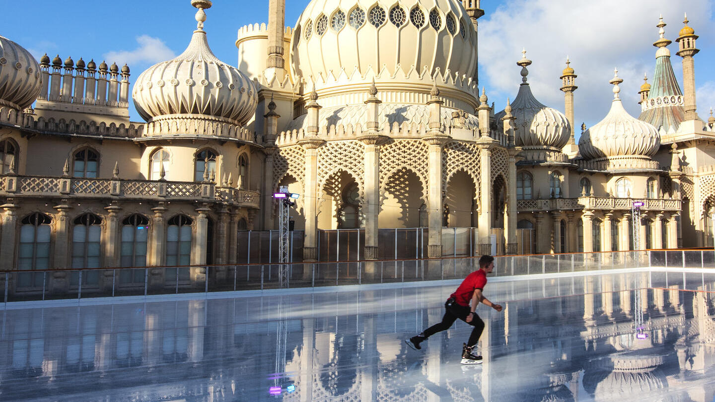 Man ice skating on a rink in front of a palace with domes and turrets