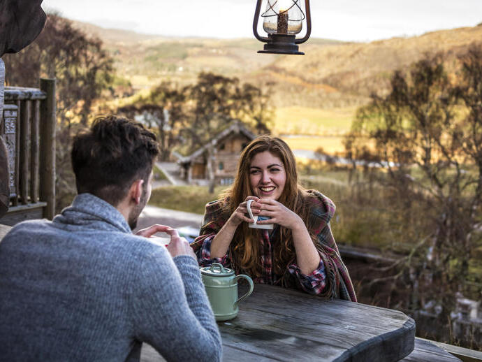 Couple sat at a wooden table drinking tea in a valley