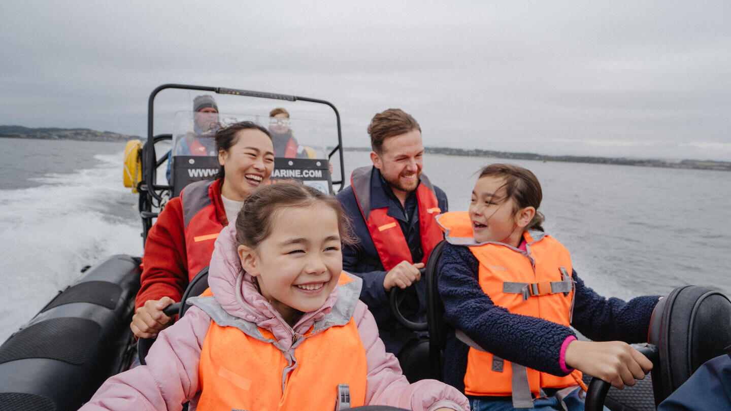 A woman, two girls and a man inside a speedboat with the crew behind them.