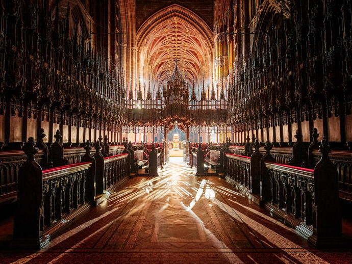 Interior of a grand gothic cathedral with ornate woodwork, high vaulted ceiling, and sunlight streaming through windows.