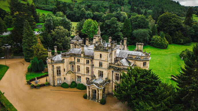 Exterior view of a large country house surrounded by green hills in the countryside