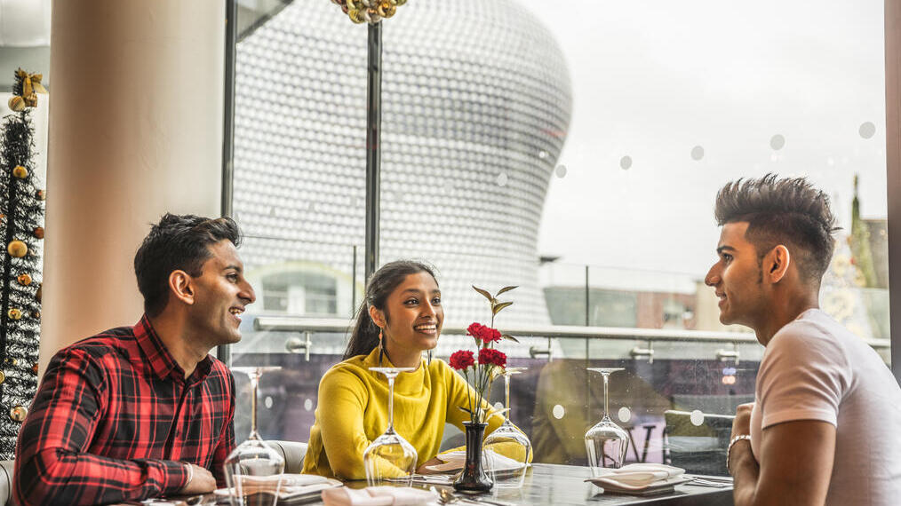 Three young people sat at a dining table with high views