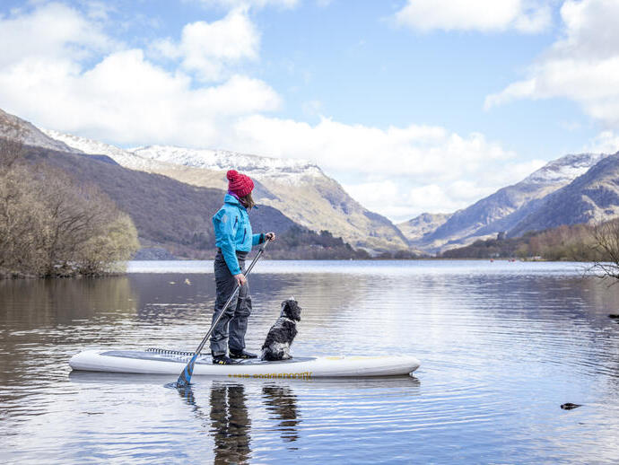 Woman and a dog on a paddleboard on a lake with mountains in the background