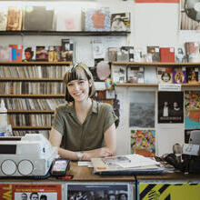 Young woman smiling, behind a counter in a record shop, with the till and card reader in front of her