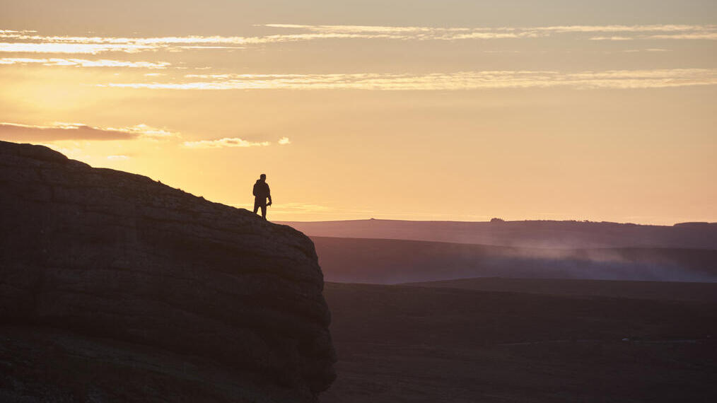 Silueta de una persona haciendo senderismo en una gran colina al atardecer