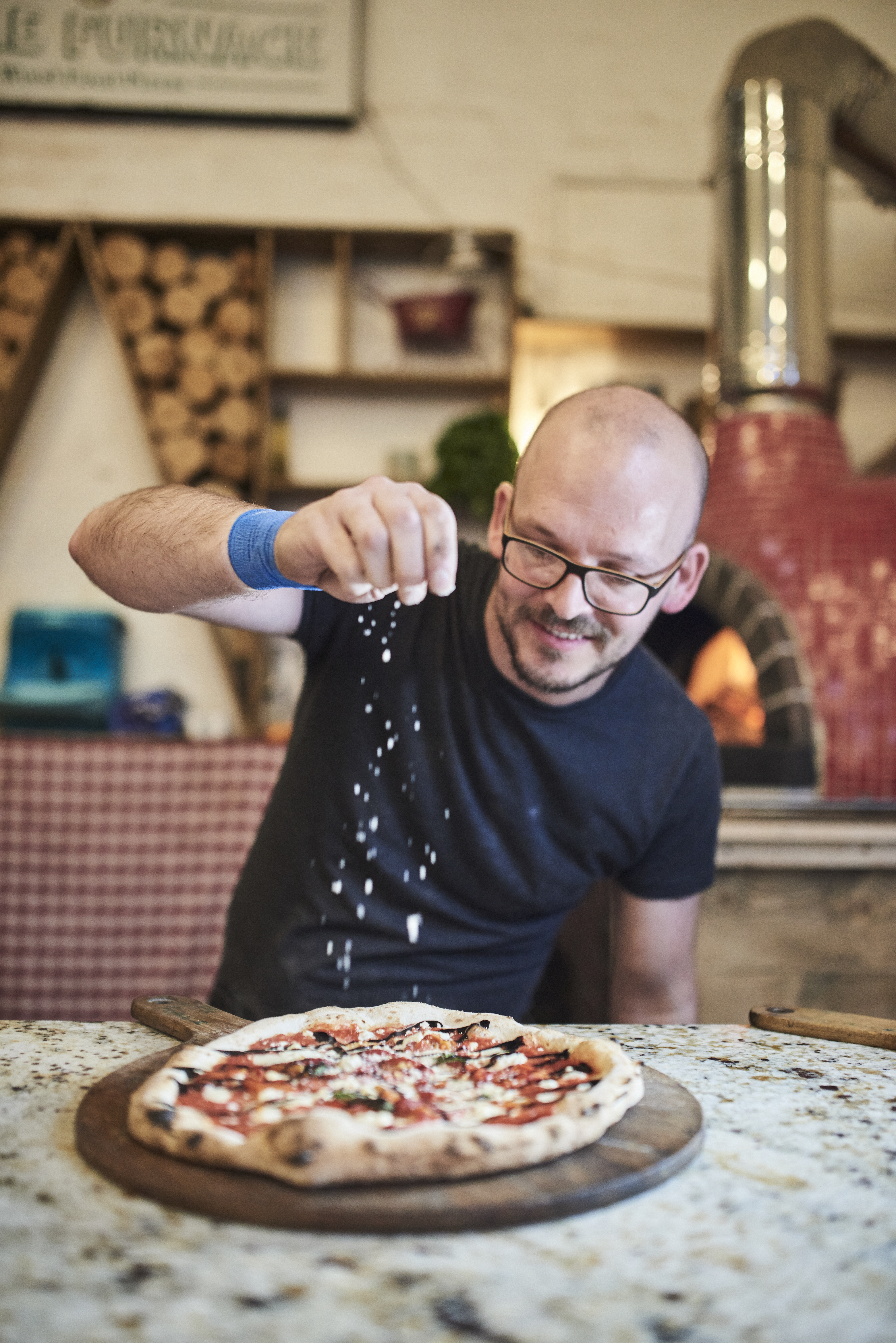 Man sprinkling cheese on pizza at a food market
