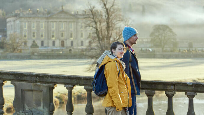 Couple walking on a stone bridge, a large country house in the backround