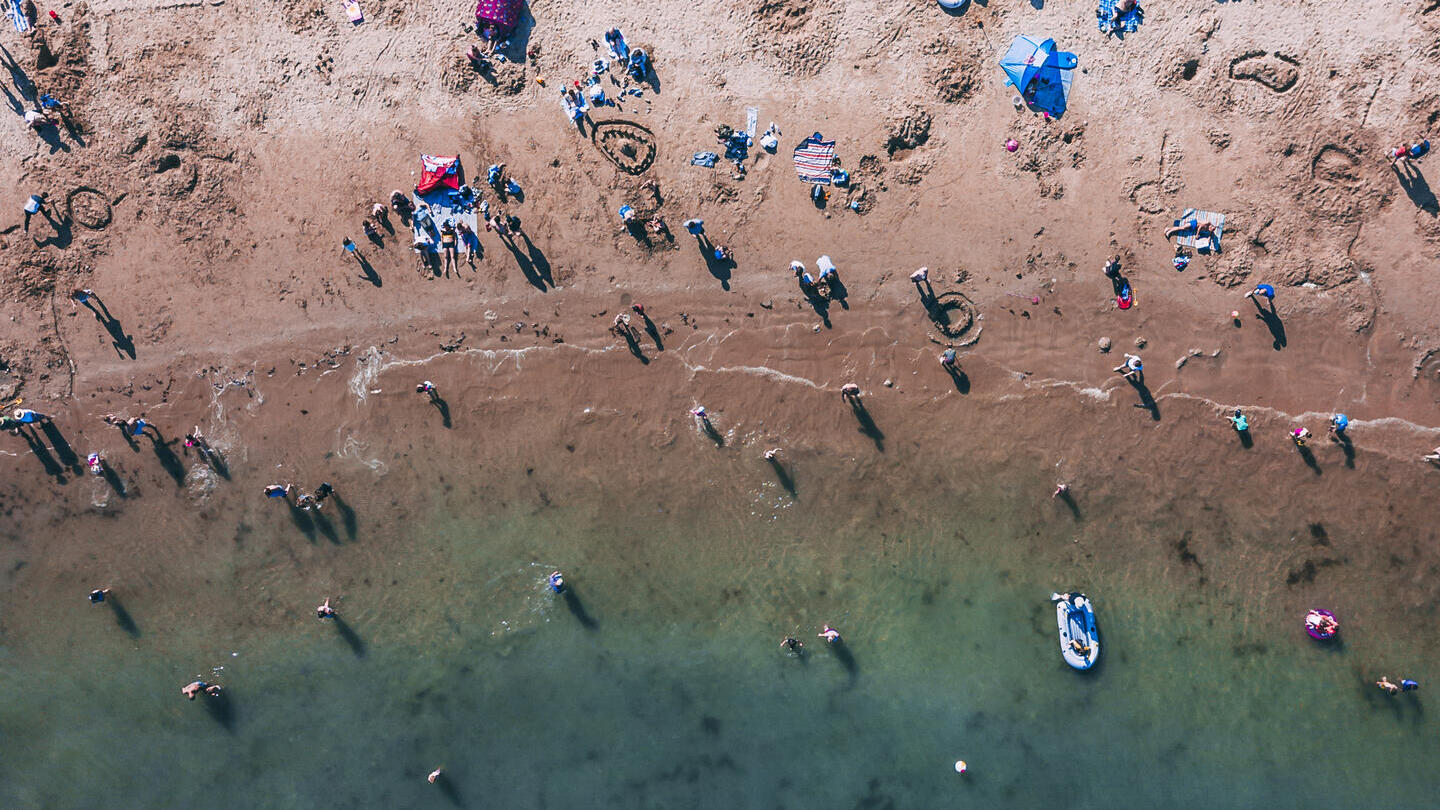 Aerial view of people on sandy beach and swimming in sea