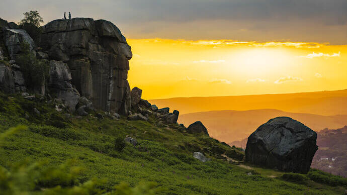A landscape with a large rock formation and a sunset beyond