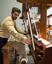 A person weaving fabric on a traditional wooden loom.
