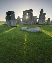 Large stone pillars arranged in circle on grass. Sunset