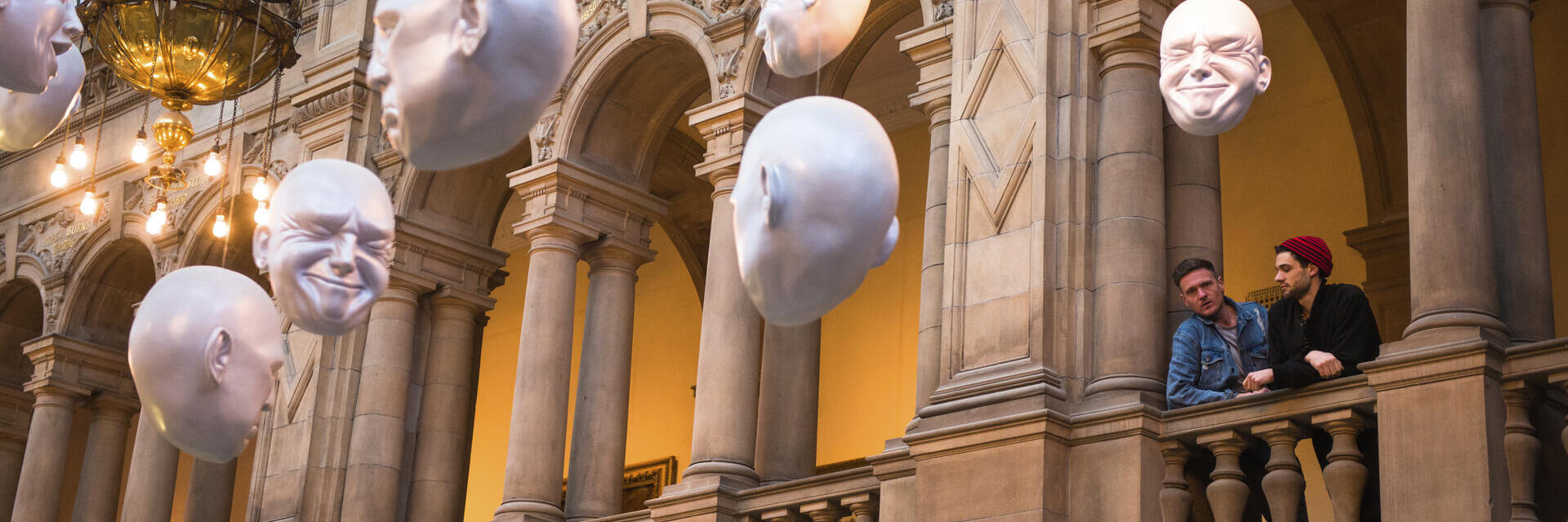 Two men looking at installation of suspended head sculptures inside a museum.