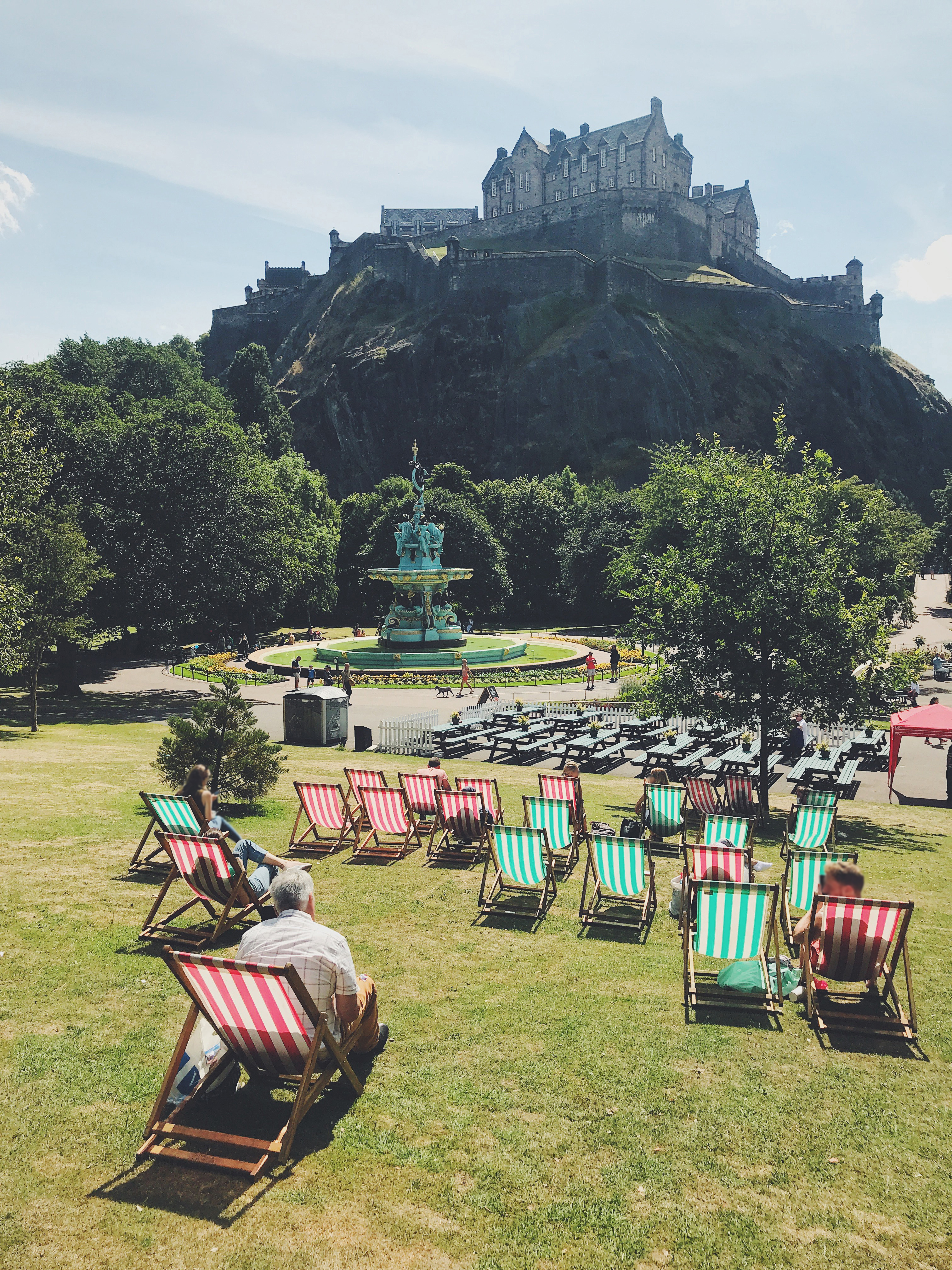 Green and red deck chairs laid out on grass in a park in front of a castle