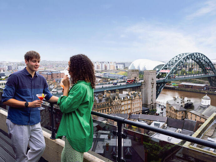 Two people enjoy drinks on a rooftop terrace with a cityscape, Tyne Bridge, and river view in Newcastle.