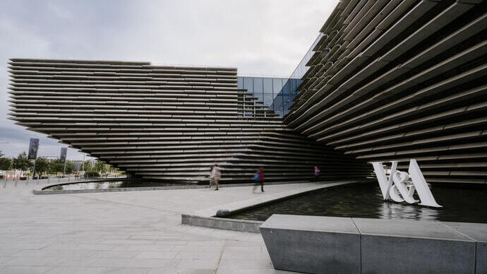 Modern building with layered concrete facade, water feature, and people walking near a large V&A sign outside.