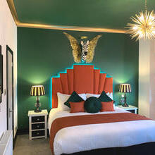 View of a bedroom with a spiky light fitting and the head of a zebra in the centre of a pair of gold wings hung above the bed.