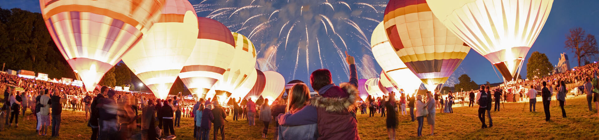Couple watching grounded hot air balloons and fireworks in the night sky