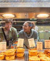 Friends admiring bakery pies through a glass divider.
