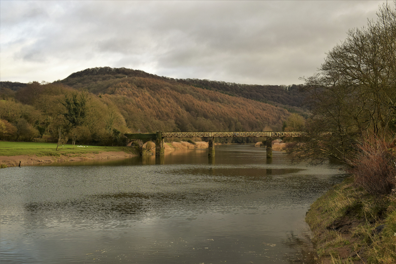 Un pont en pierre et en métal rouillé enjambant une large rivière dans la campagne en automne.