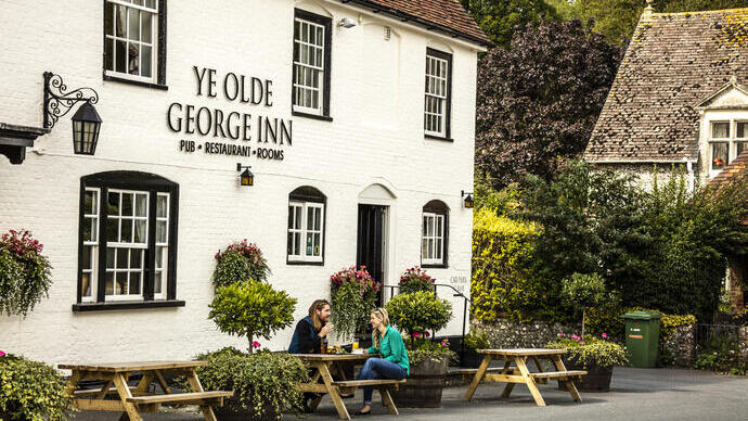 A couple sitting outside a pub on a bench having a drink and eating a meal